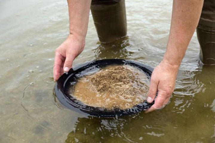 Où chercher de l’or en Pologne ? 1 Orpailleur utilisant une batée noire pour trier le sable et les graviers dans l'eau d'une rivière en Pologne.